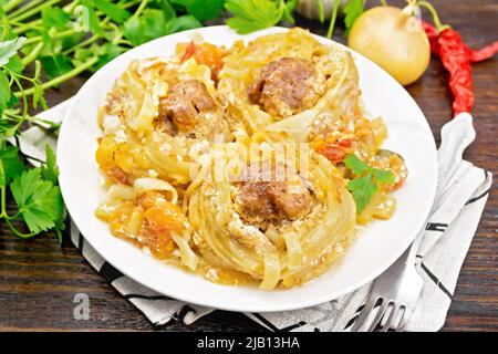 Twisted pasta with meatballs in the center with cream sauce, stewed tomatoes, peppers, onions and garlic in white plate on wooden board background Stock Photo