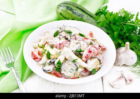 Salad with fried zucchini, boiled egg, fresh tomato and garlic, dressed with mayonnaise in plate, napkin and parsley on white wooden board background Stock Photo