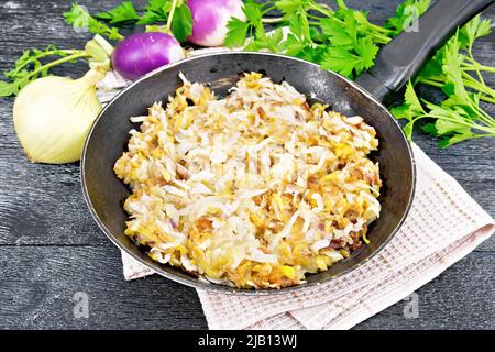 Fried turnips with onions in a frying pan on a towel on black wooden board background Stock Photo