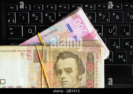 Ukrainian one hundred and two hundred hryvnia lie on the laptop keyboard, work on the Internet, income and profit, Ukrainian hryvnia Stock Photo