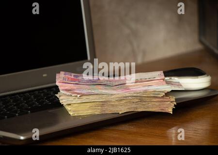 Ukrainian one hundred and two hundred hryvnias lie near a laptop on the table at home, work on the Internet, income and profit, Ukrainian hryvnias Stock Photo