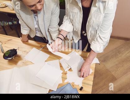 Top view of sewing patterns and blue fabric on a wooden desk and two seamstresses, tailors, clothing designers working on creating new garment in fash Stock Photo