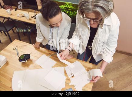 Two stylish women of diverse nationalities and ages discussing sewing patterns while developing a new collection of clothes in a fashion design worksh Stock Photo