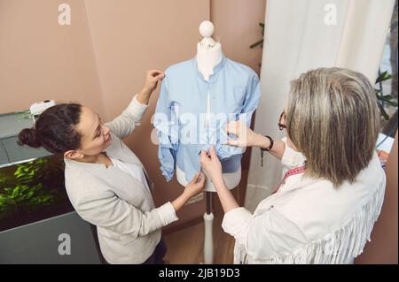 View from above to a team of multi-ethnic and diverse female fashion designers tailors trying on a handmade classical shirt from new collection on man Stock Photo
