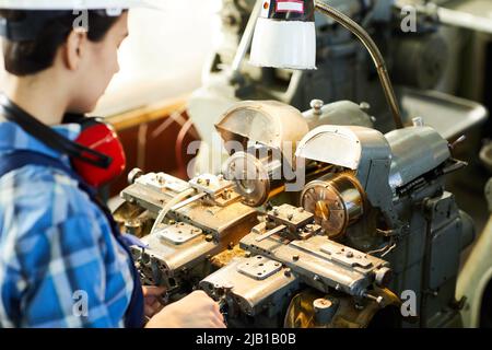 Over shoulder view of busy female engineer adjusting lathe machine for designing details at wristwatch factory Stock Photo