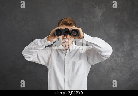 Happy young man who's searching for something is holding binoculars and looking forward Stock Photo