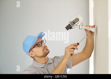 Concentrated young male technician repairs or installs CCTV system on wall inside building. Stock Photo