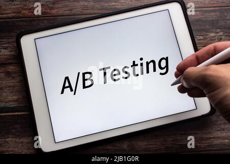 Tablet displaying “A/B Testing” on white background. Man holding stylus pen in image. A/B testing is a user experience research methodology Stock Photo