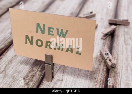 Conceptual message “New Normal” on shabby wooden table in retro mood. Natural wooden pinch holding paper note. Covid-19 and coronavirus concept. Stock Photo