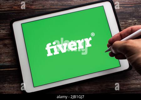 Kumamoto, JAPAN - May 13 2021 : Logo of Fiverr, an Israeli online marketplace for freelance services, on tablet. Man hand holding wireless stylus pen. Stock Photo