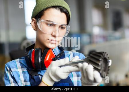 Serious thoughtful attractive female engineer in transparent safety goggles examining milling machine tool while finding out reason of breakage Stock Photo
