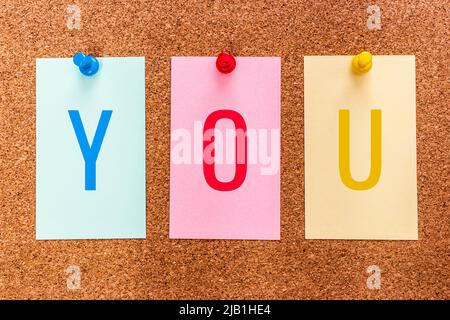 Conceptual 3 letter keyword YOU on multicolored stickers attached to a cork board. Stock Photo