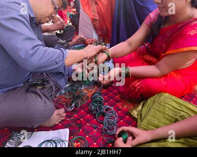 17 May 2022, Pune, India, Pre wedding ceremony a lady bangle seller is putting green glass bangles, Indian culture. Stock Photo