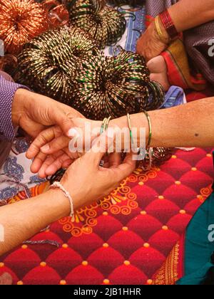 Pre wedding ceremony a lady bangle seller is putting green glass bangles, Indian culture. Stock Photo