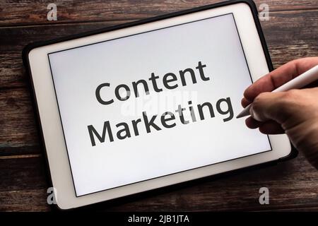 Keyword Content Marketing on tablet. A way of marketing focused on creating, publishing, & distributing content for a target user. Man holding a pen Stock Photo