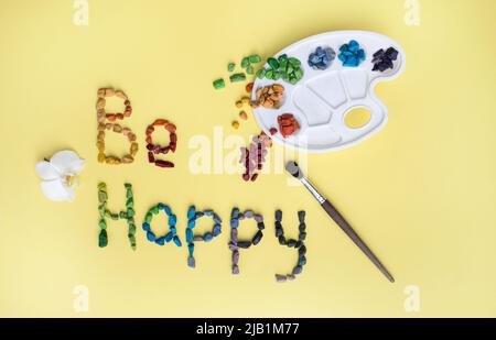 wish to be happy is written from multi-colored candies in the form of sea pebbles, a palette for watercolor, a brush on a yellow background. Birthday Stock Photo