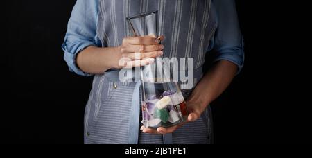 Woman holding healthy water stones in a carafe with Rock crystal, rose quartz and amethyst on black background, for wellness concepts. Stock Photo