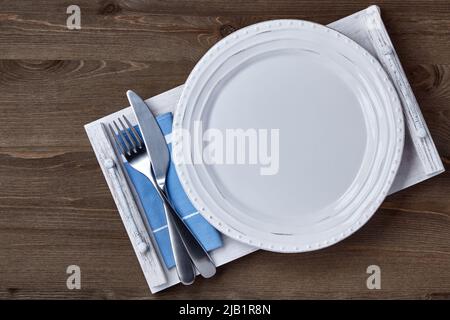 Empty ceramic white plate with cutlery on a napkin on a white wooden tray on a brown table. Menu layout Stock Photo