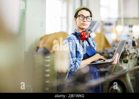 Serious confident female industrial worker in glasses using laptop to watch online 3D maquette, she looking at camera Stock Photo
