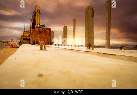 Selective focus on bucklet of old backhoe. Digger parked at construction site. Bulldozer near concrete pole. Earth moving machine. Yellow digger Stock Photo