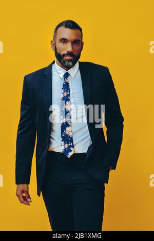 portrait of handsome bearded gentleman in suit and tie, isolated on yellow background hand in pocket studio Stock Photo