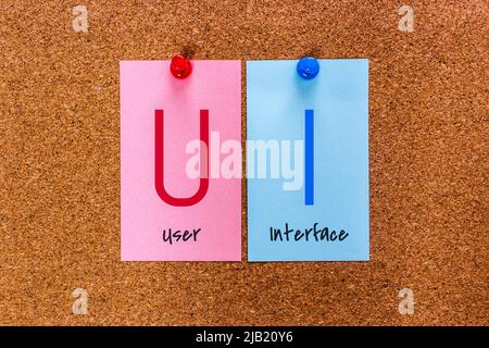 Conceptual 2 letters keyword UI (User Interface) on multicolored stickers attached to a cork board. Stock Photo