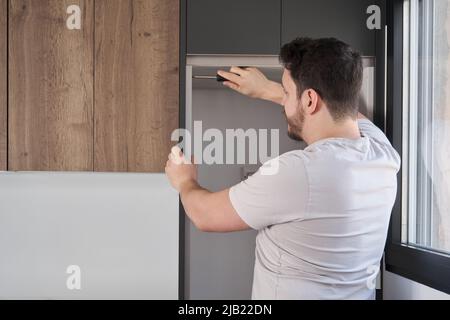 Young hispanic man installing furniture in the kitchen using a screwdriver. Stock Photo