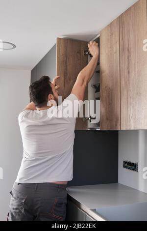 Young hispanic man installing furniture in the kitchen using a screwdriver. Stock Photo
