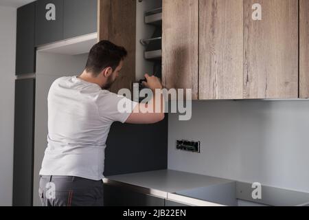 Young argentinian man installing cabinet in the kitchen using a screwdriver. Stock Photo