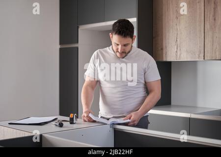 Young latin man read instruction manual before installing furniture on kitchen. Stock Photo