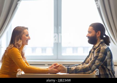 Beautiful couple having a conversation while looking at each other over a window background in a bright room Stock Photo