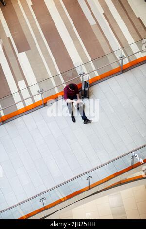 Directly above view of busy young man sitting on floor in airport lobby and typing on laptop while working remotely Stock Photo