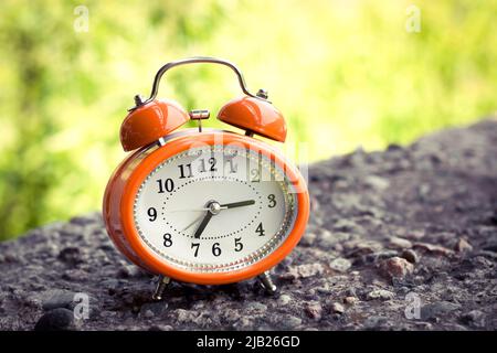 Vintage style orange alarm clock on a concrete surface. Stock Photo