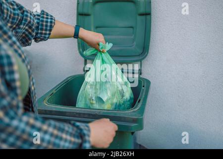 European 30s woman throwing garbage into the recycling bin in the backyard near the house. Separating recyclable garbage plastic  Stock Photo