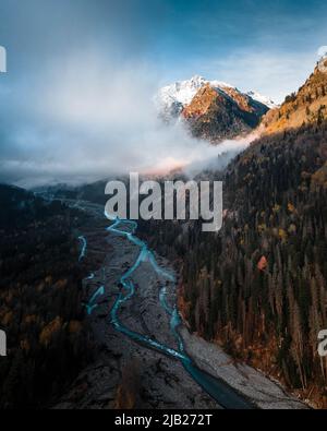 wild mountain river flows between trees under low clouds Stock Photo