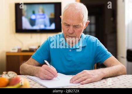 Focused senior man sitting at home reading and signing papers Stock Photo