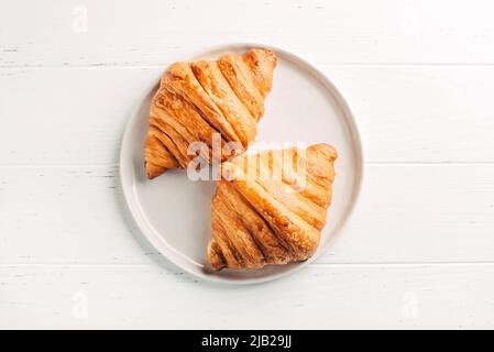 Plate with two fresh croissants on white table. Stock Photo