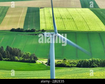 A lateral perspective of a wind farm turbine constructed within a rural countryside region, positioned within an agricultural field. Stock Photo