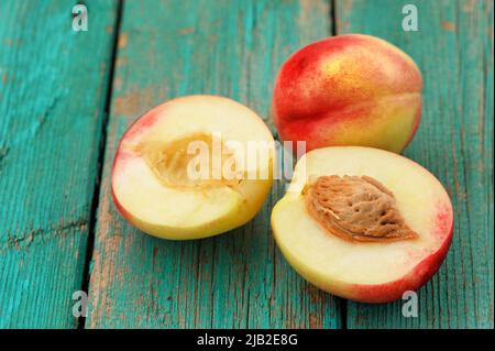Two fresh nectarines, whole and split with stone, on vintage turquoise table closeup horizontal Stock Photo