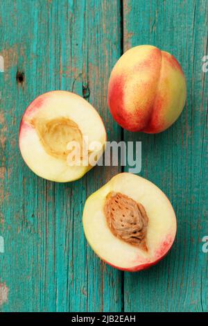 Two nectarines, whole and split on vintage turquoise table vertical Stock Photo