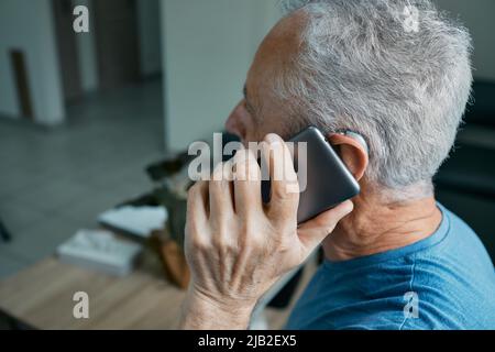 Elderly man with hearing aid has a full life and can hear interlocutor on phone. Hearing solution and innovation technology Stock Photo