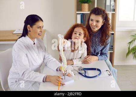 Little cute girl examines anatomical model of spine who is standing on table in doctor's office. Stock Photo