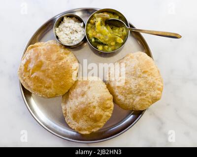 Puri served with bhaji and chutney placed in a serving plate and placed on a marble top table. Stock Photo