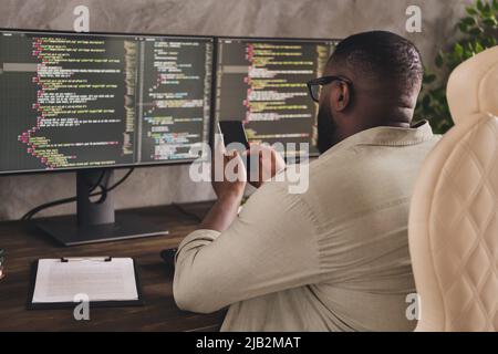 Rear back behind view portrait of handsome focused guy using device gadget chatting at workplace workstation indoors Stock Photo