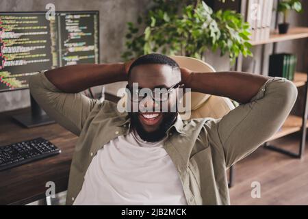 Portrait of attractive cheerful guy expert technician tech support sitting in armchair at workplace workstation indoors Stock Photo