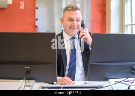 Confident businessman talking on a phone in an office viewed between computers as he smiles at the camera Stock Photo