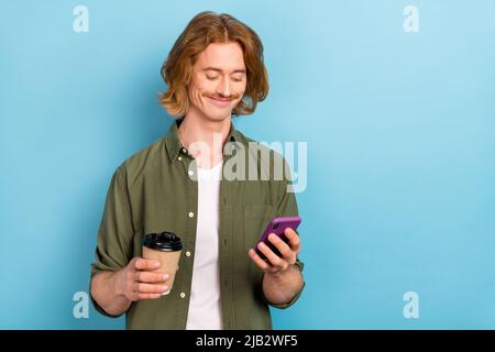 Portrait of attractive focused cheerful guy drinking latte using device copy space isolated over pastel blue color background Stock Photo