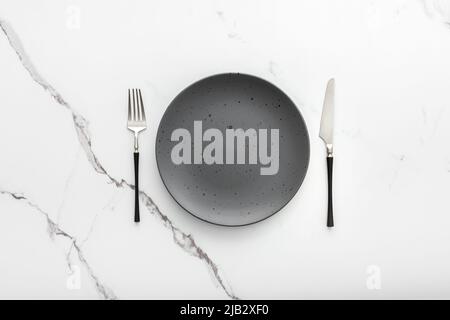 Table setting, empty plate with cutlery on a marble background, top view of the served table Stock Photo