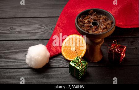 hookah bowl with tobacco with a Christmas red hat on a dark background. Christmas accessories Stock Photo