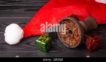 hookah bowl with tobacco with a Christmas red hat on a dark background. Christmas accessories Stock Photo